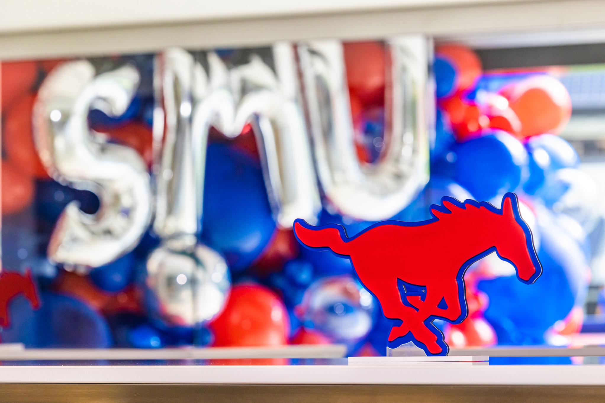 cutout of red mustang sitting on white table with silver s, m, and u letter balloons and red and blue round balloons in the background