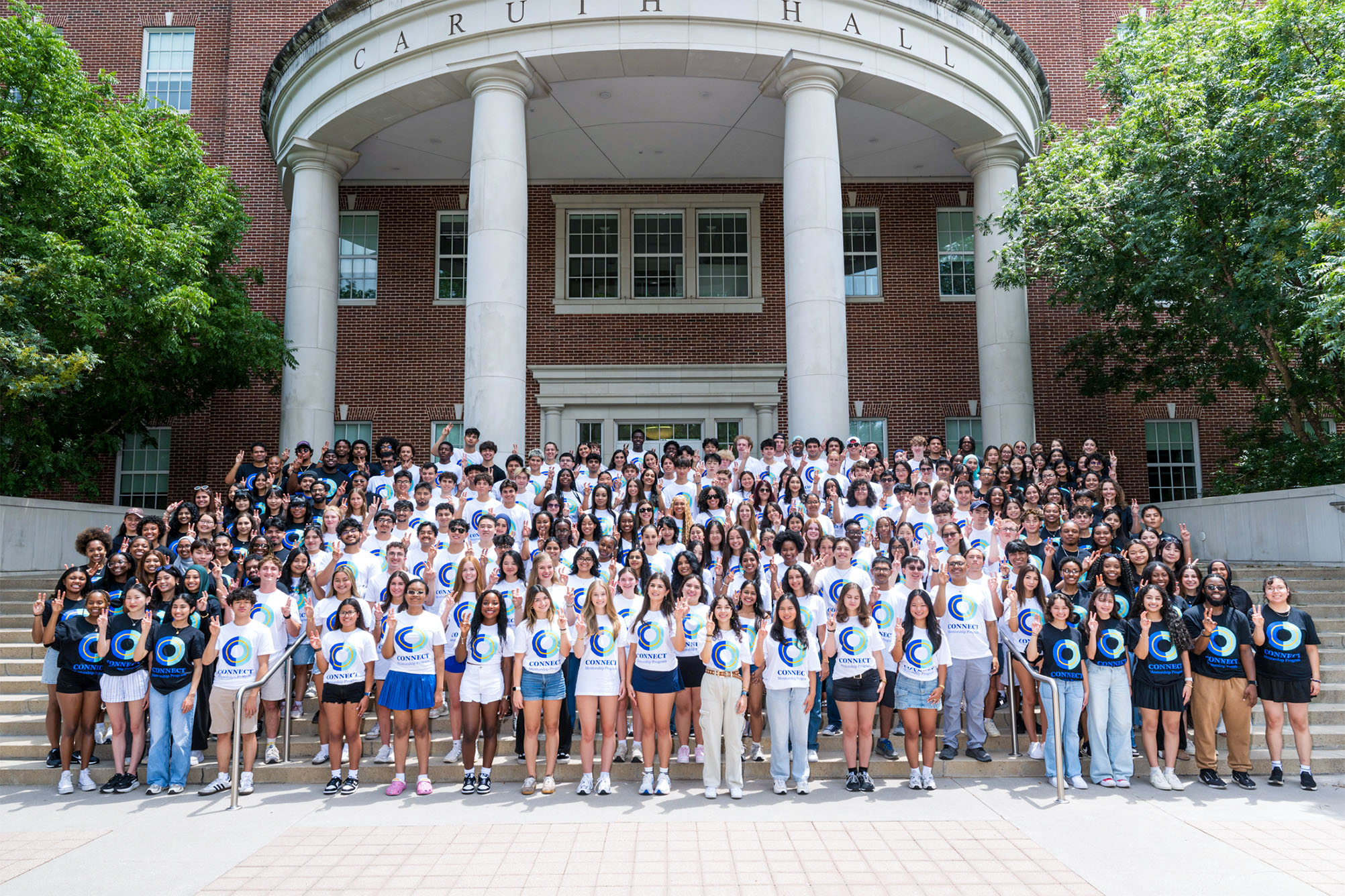 large group of students in black and white t shirts standing in front of brick building on steps for photo