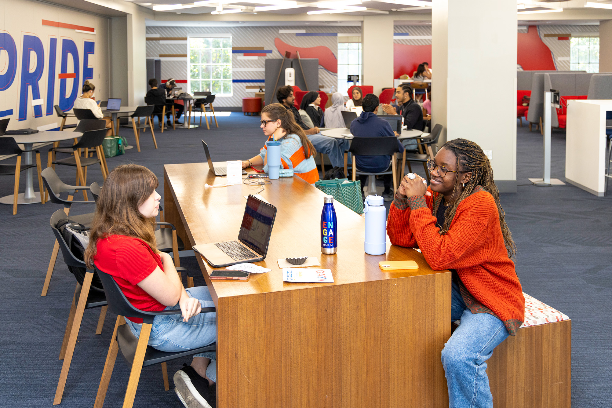 students talking at table in common area with more people in the background