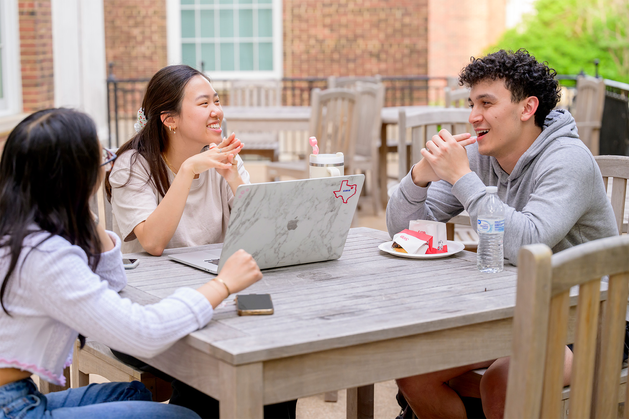three students outside sitting table working together and talking