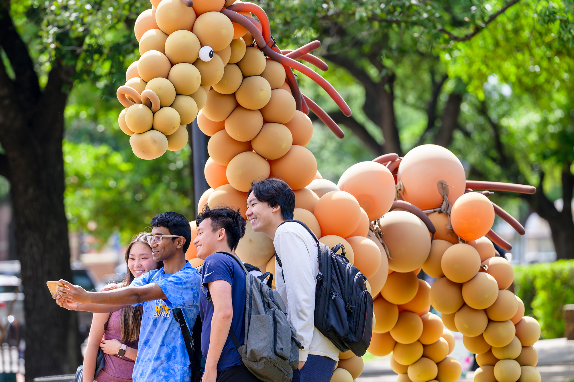 small group of students taking a picture of themselves in front of tall brown horse made of balloons