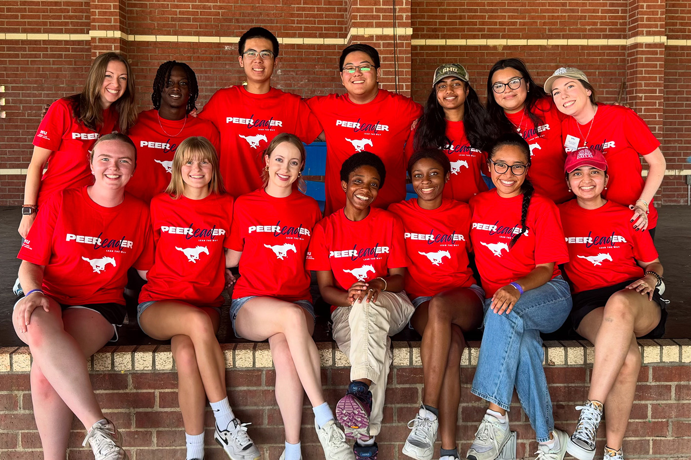 group of people in red shirts posing for photo in front of brick wall