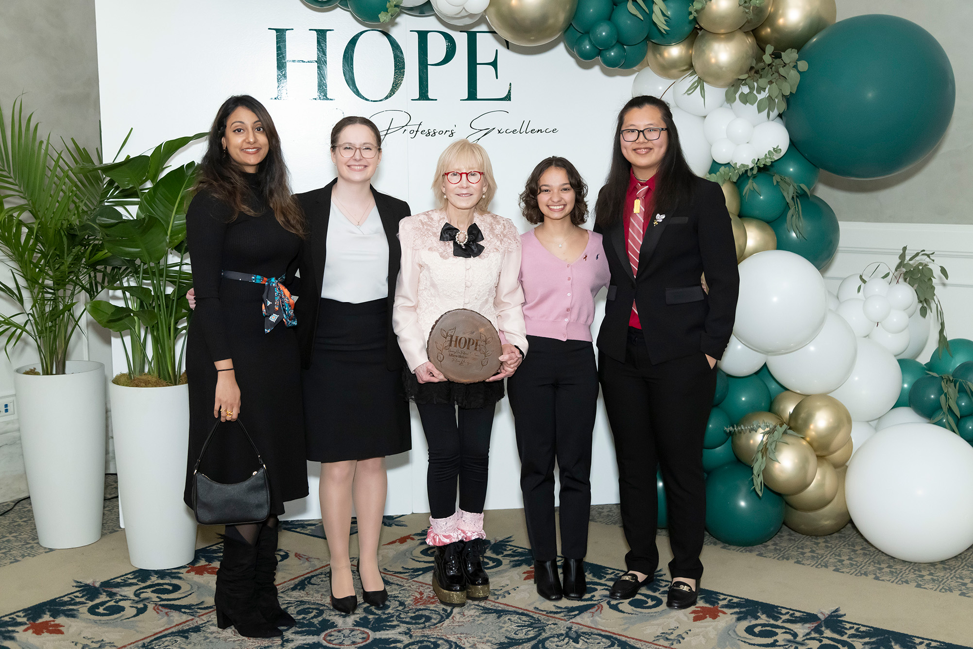 five people posing for photo with green, white, and gold balloons and trees in background