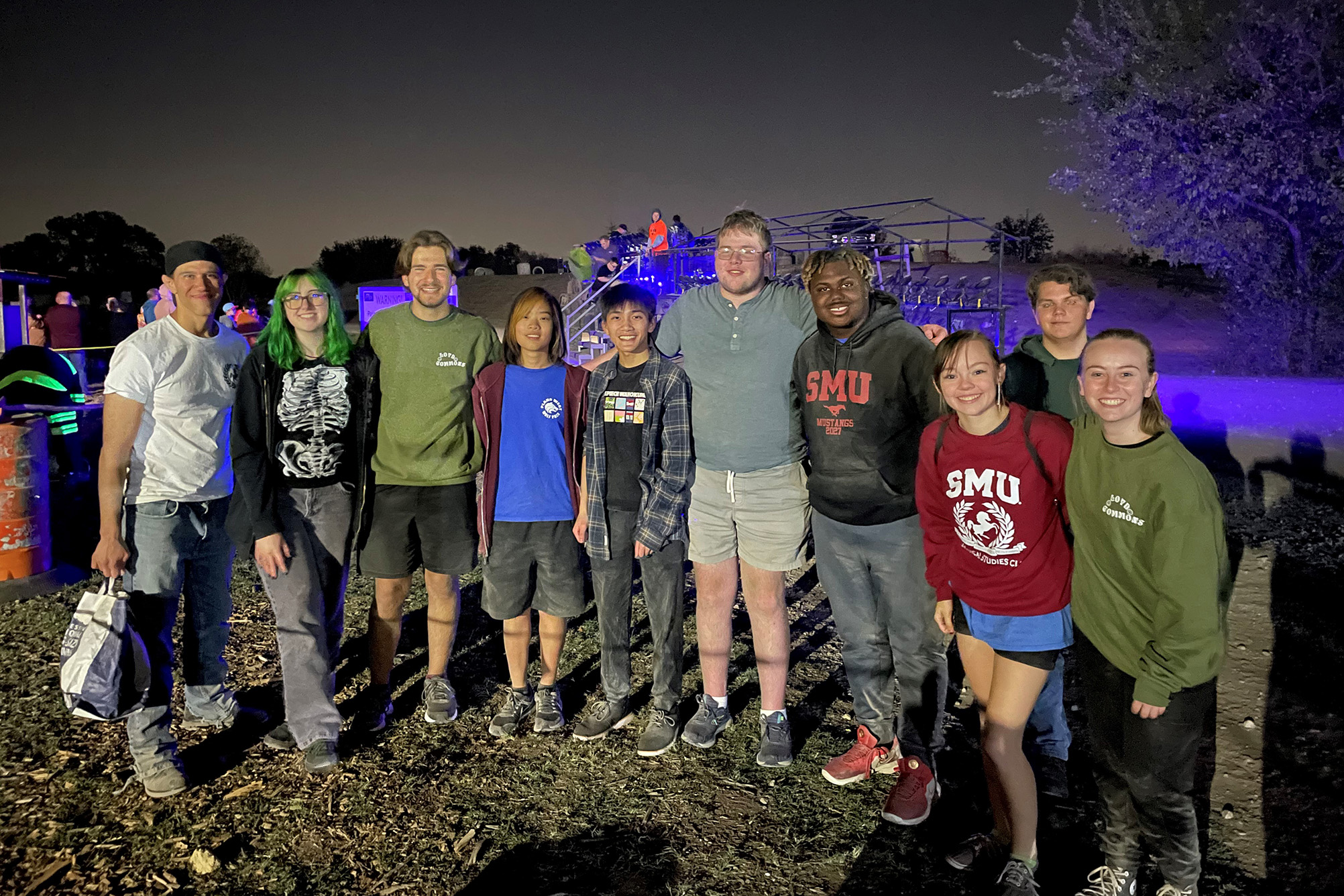 group of people outside at night after an event with purple light shining in background
