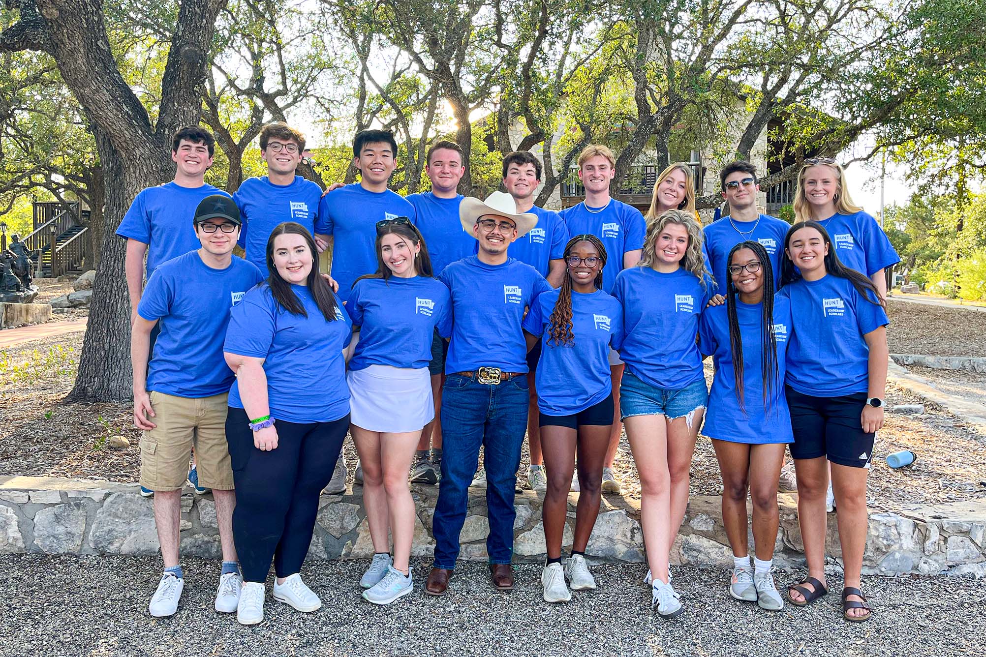 large group of students in blue tshirts standing outside for a photo in front of trees