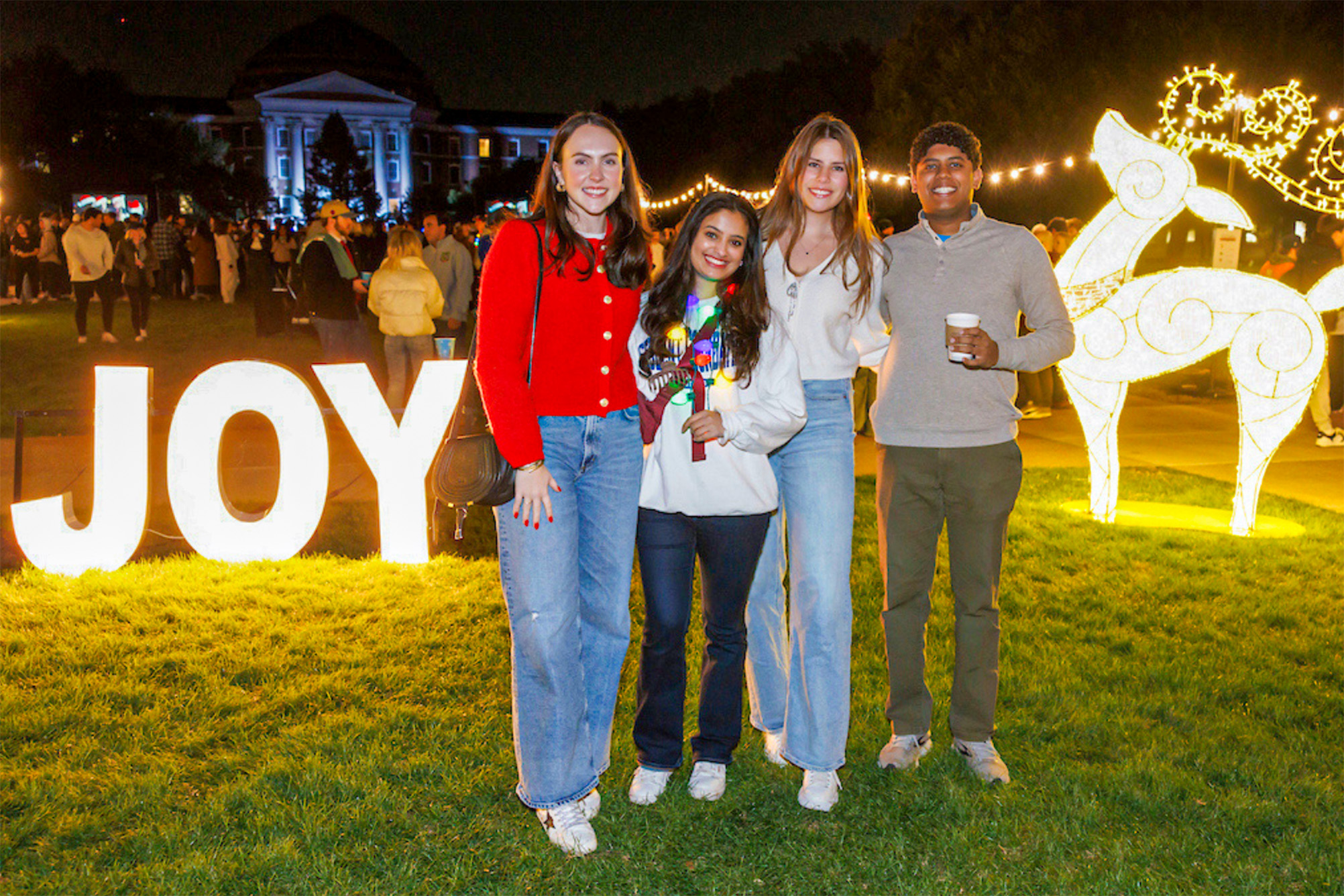 small group of people standing outside at night in front of lit up holiday yard decorations