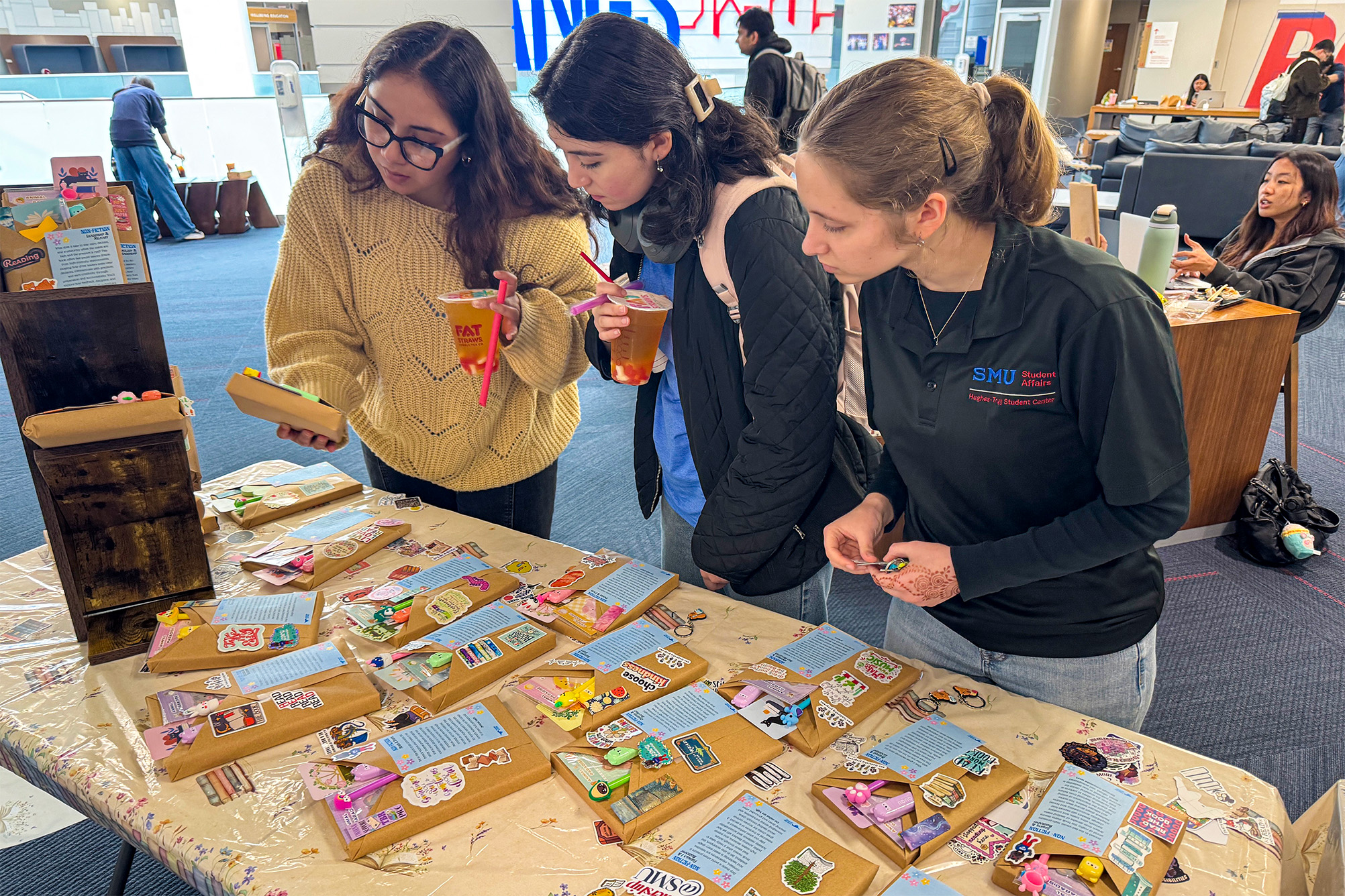three students standing at table looking at books covered in brown craft paper
