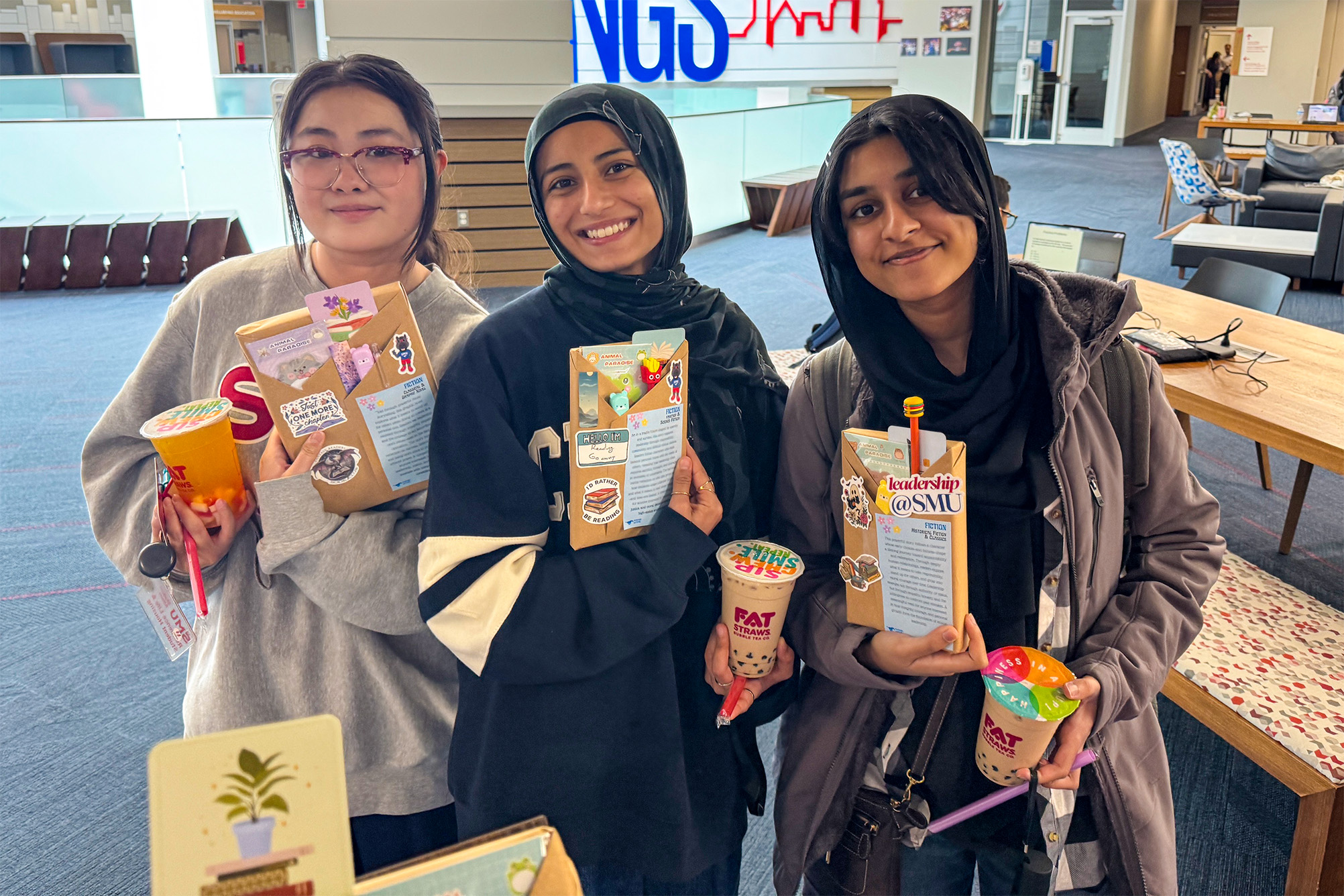 three students posing for photo with with books and drink in hand