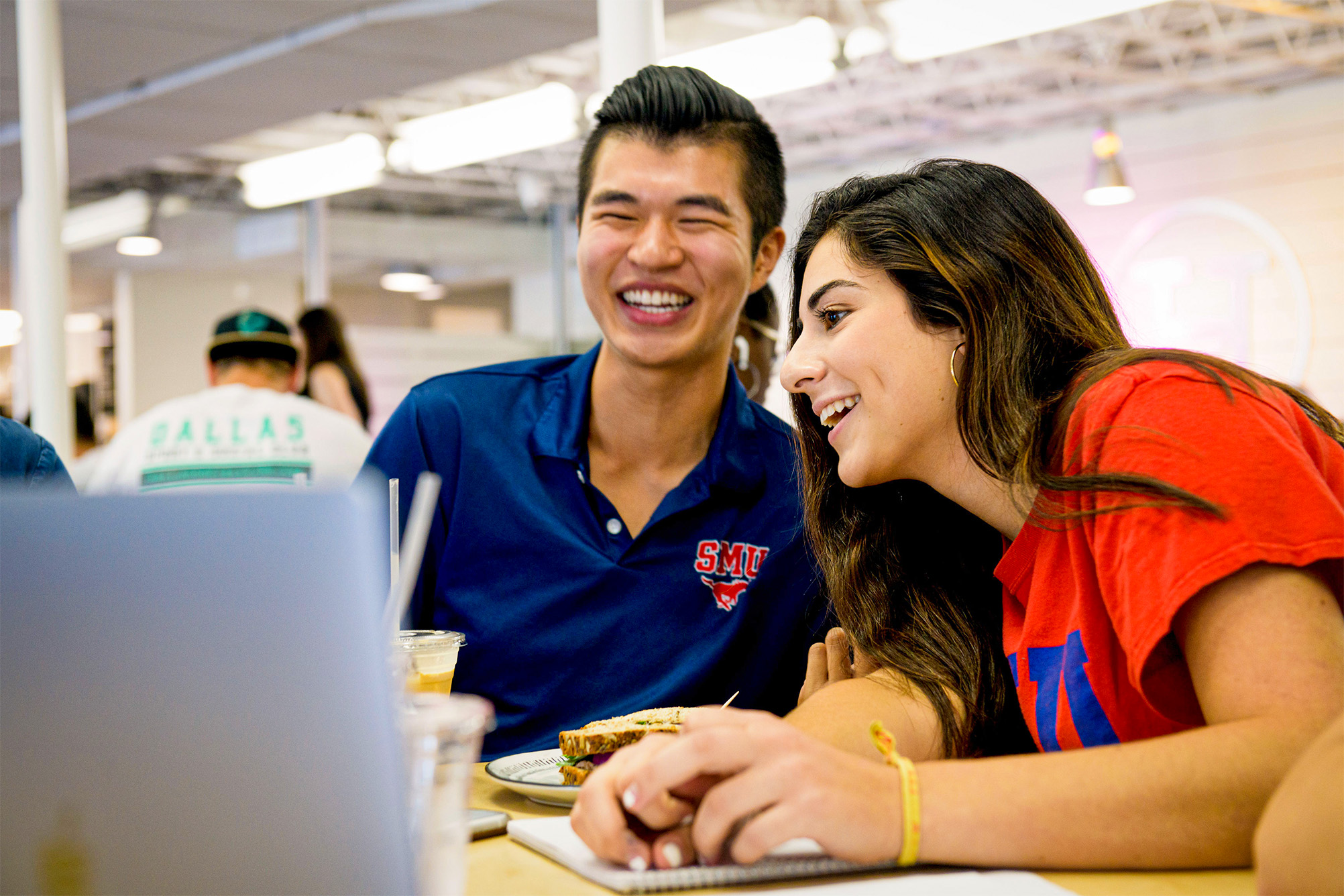 two students smiling and talking at table with laptop