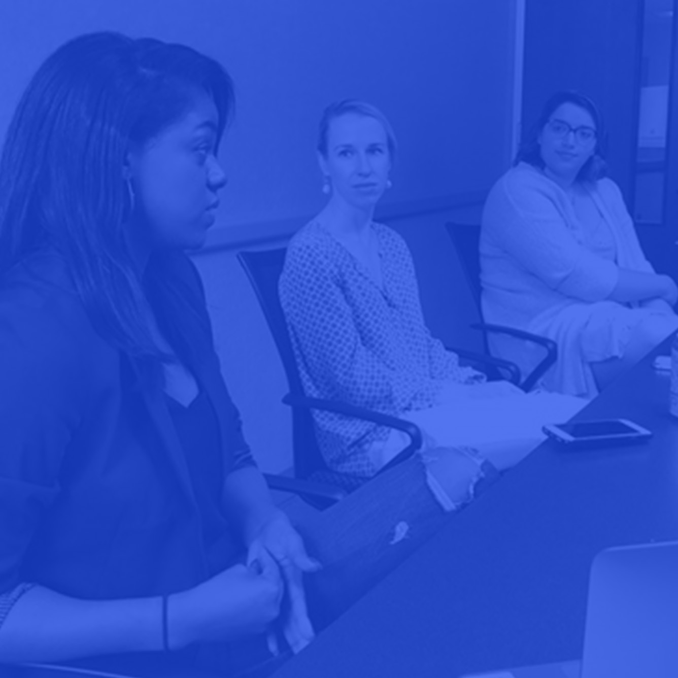 photo of students sitting at table talking with a blue color overlay on photo