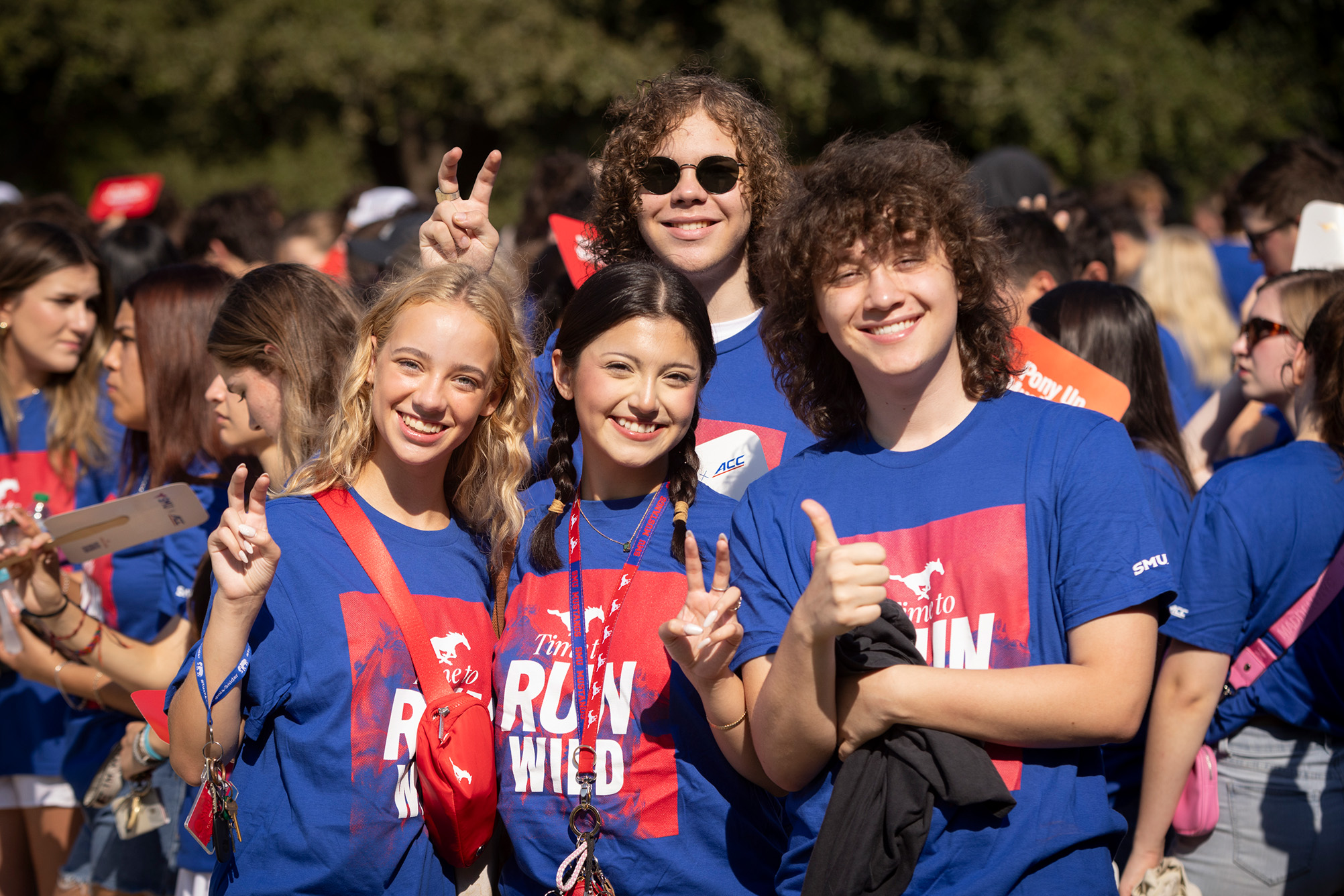 four students in blue shirts smiling at camera outside