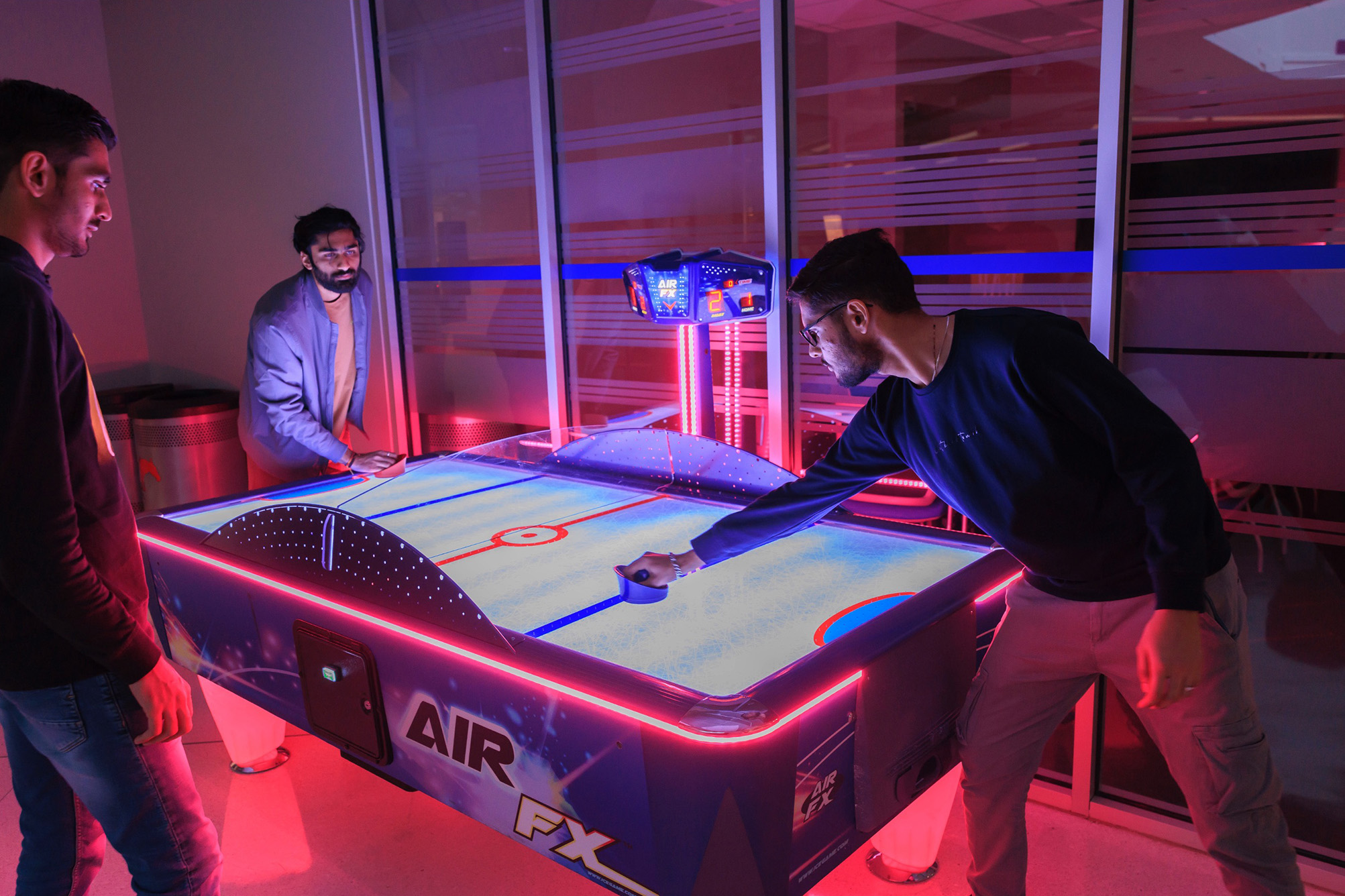 three people playing air hockey in a dark room with glowing lights