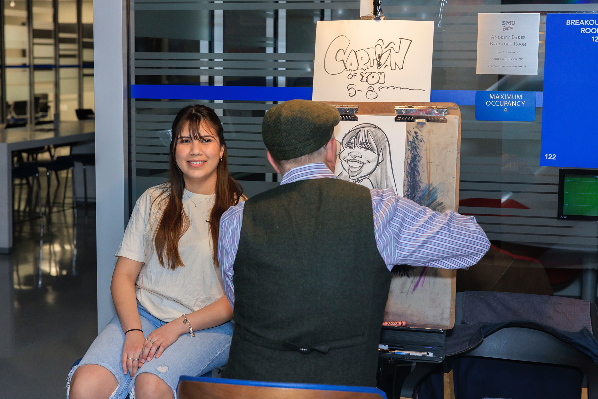 girl sitting in chair facing camera with artist drawing her picture and sitting with back to camera