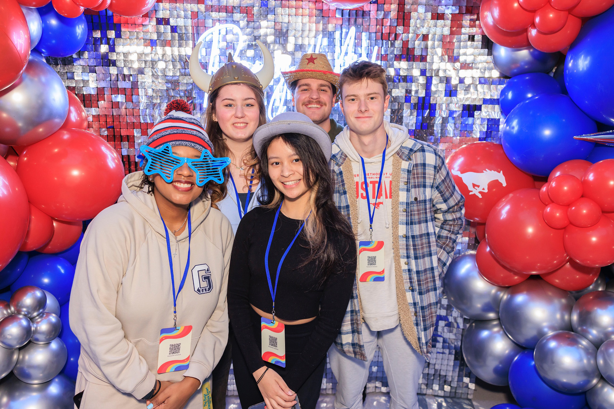 five students posing for photo in front of silver backdrop with red, blue, and sliver balloons