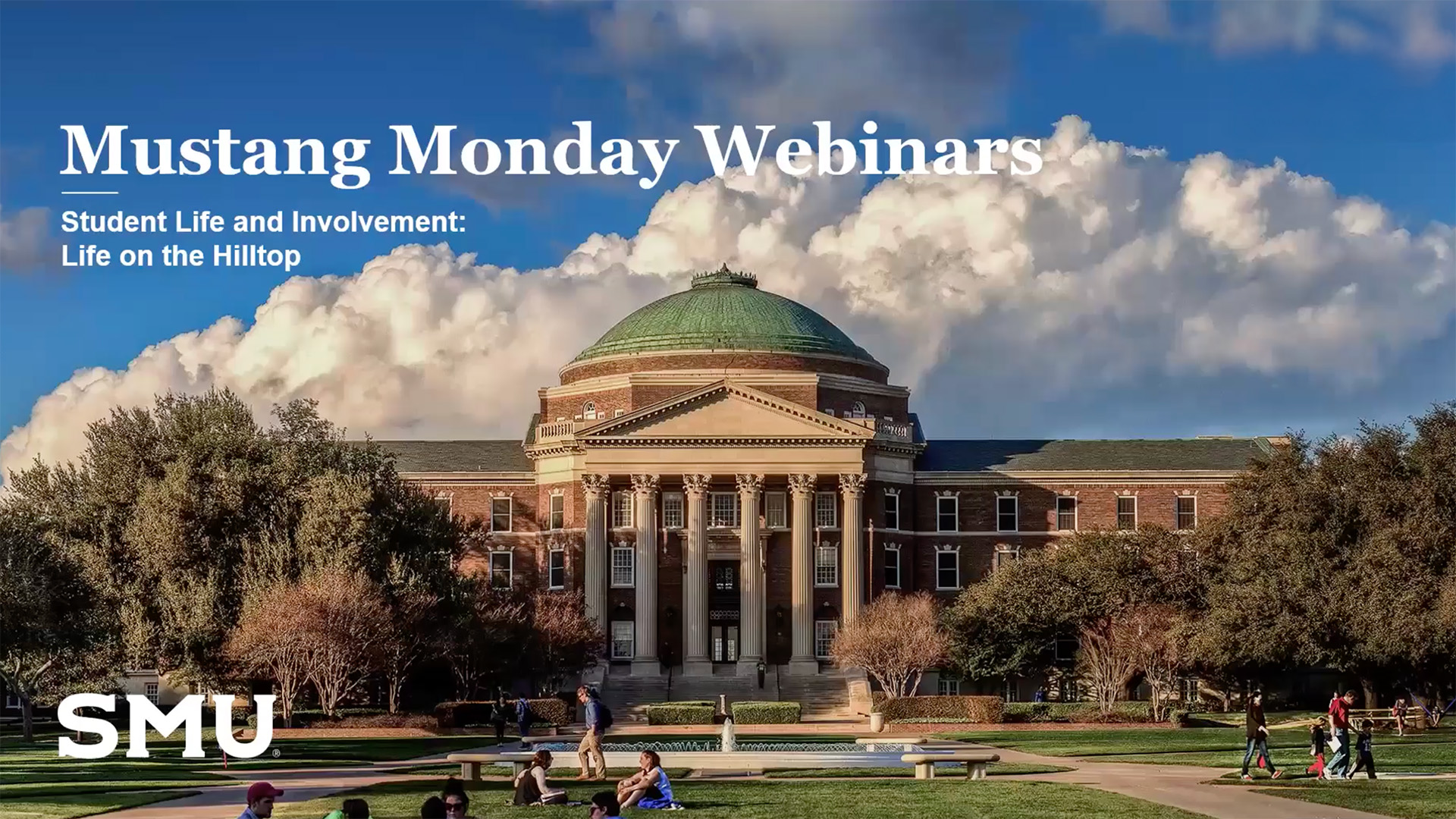 Dallas Hall with blue sky and clouds in the background, trees lining the sides of the building, and people gathered outside on the lawn