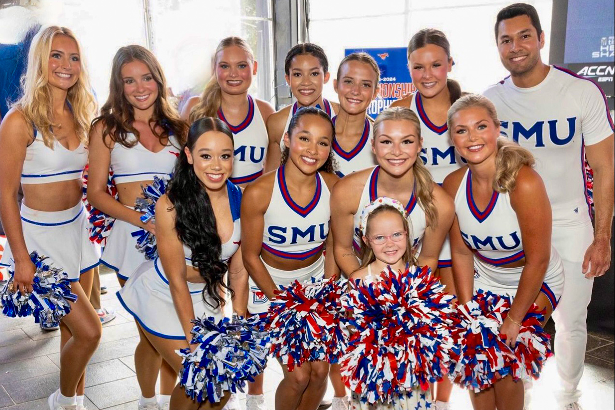 pom squad and cheerleaders in white uniforms and red, blue, and silver pompoms at event with child