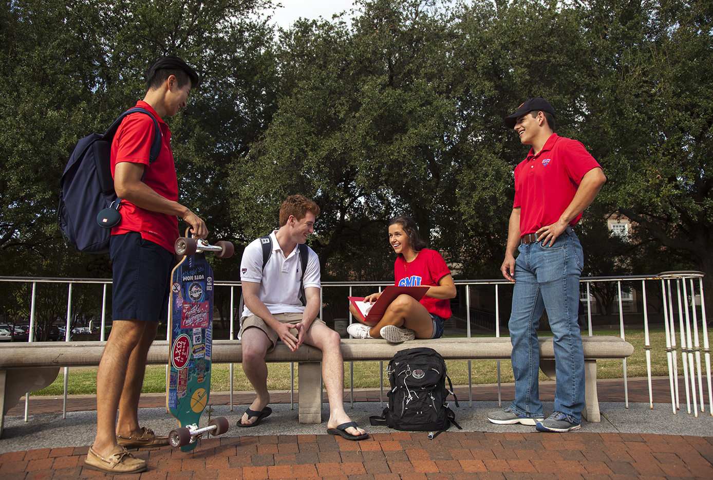 Four students, two standing and two seated on bench. 