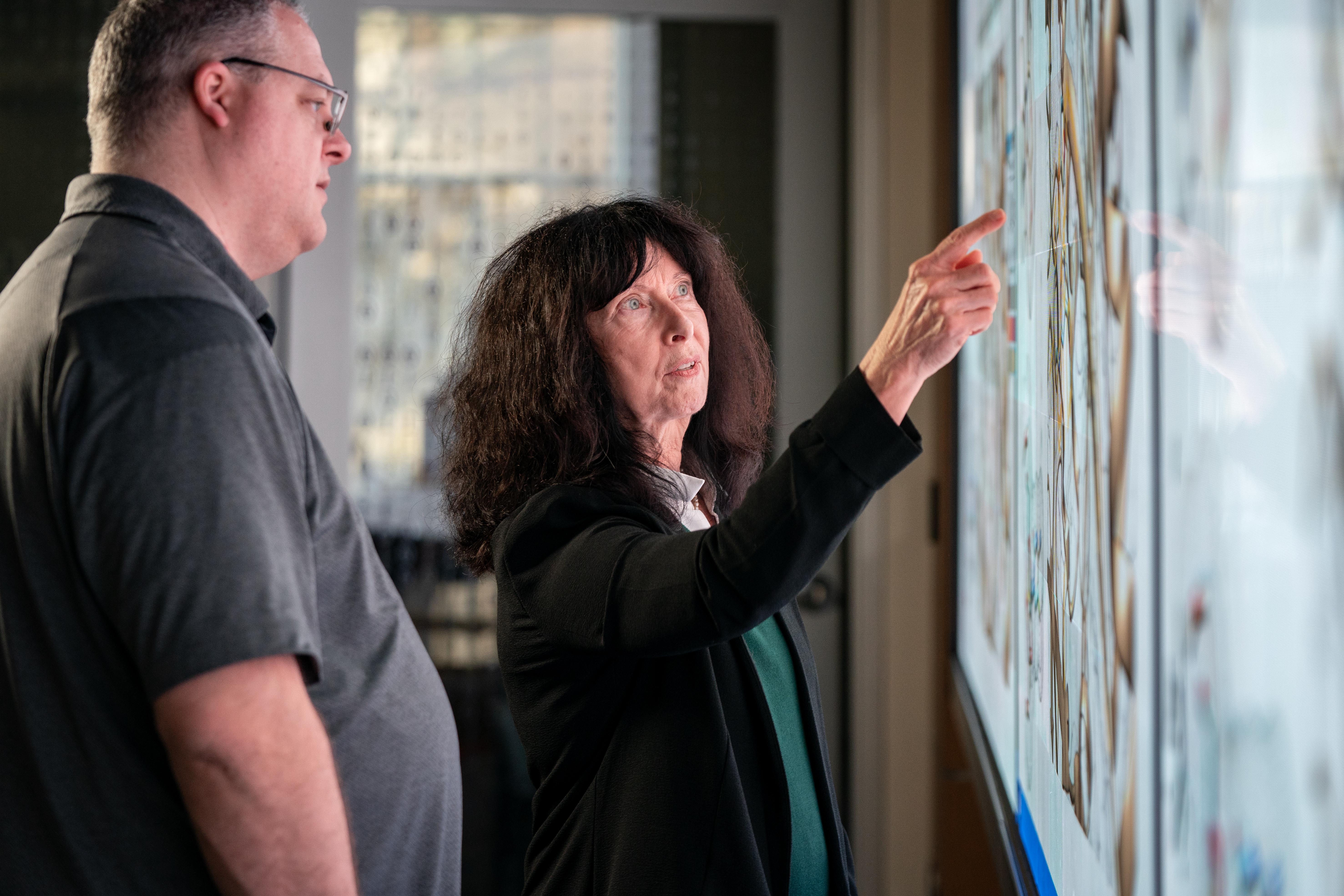 Two researchers work together at a large digital display